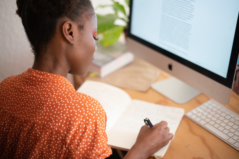 Women writing on paper with computer